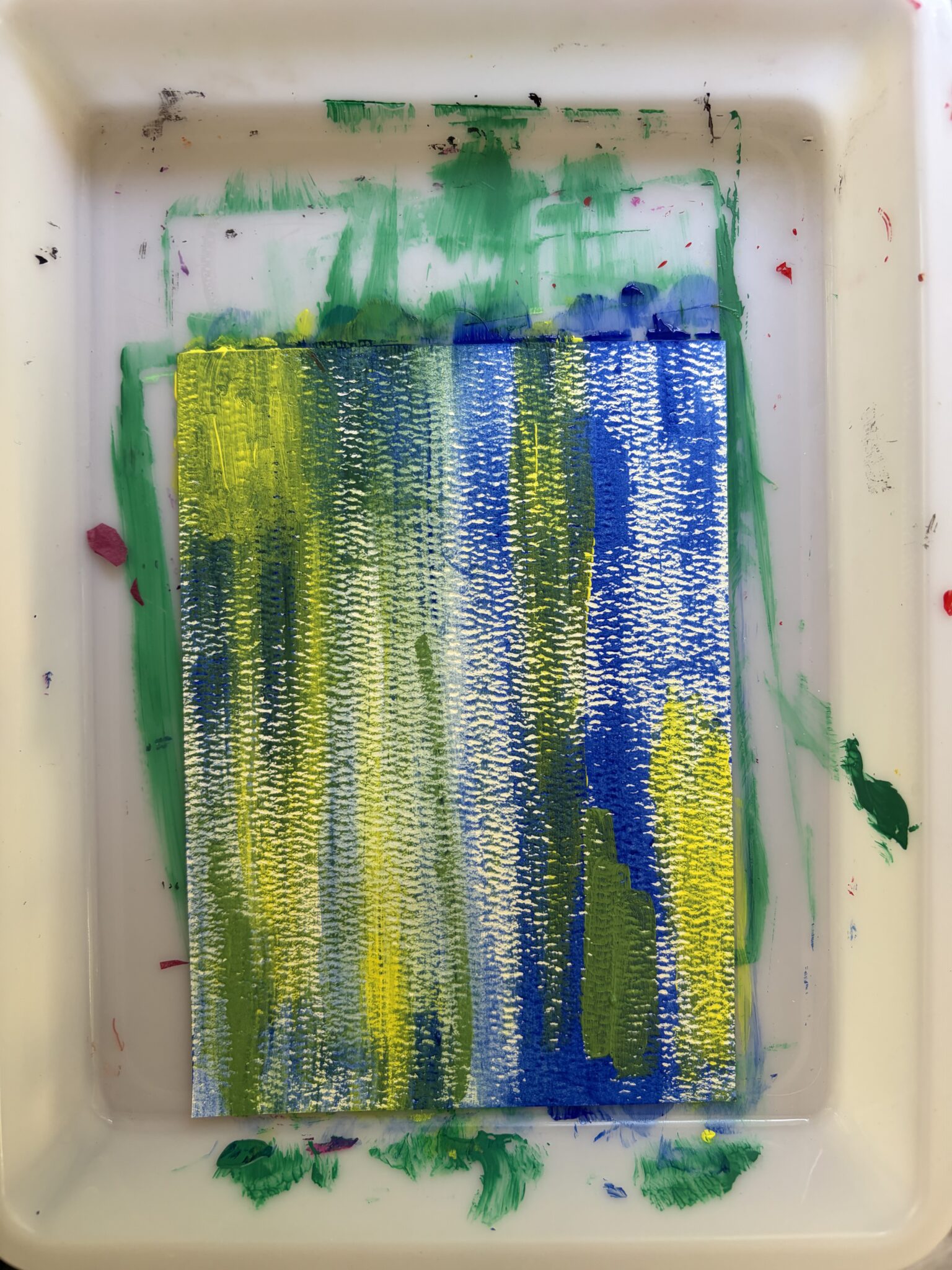 Abstract studio artwork showing dense vertical washes of emerald green, blue, and light yellow acrylic paints on heavy paper.