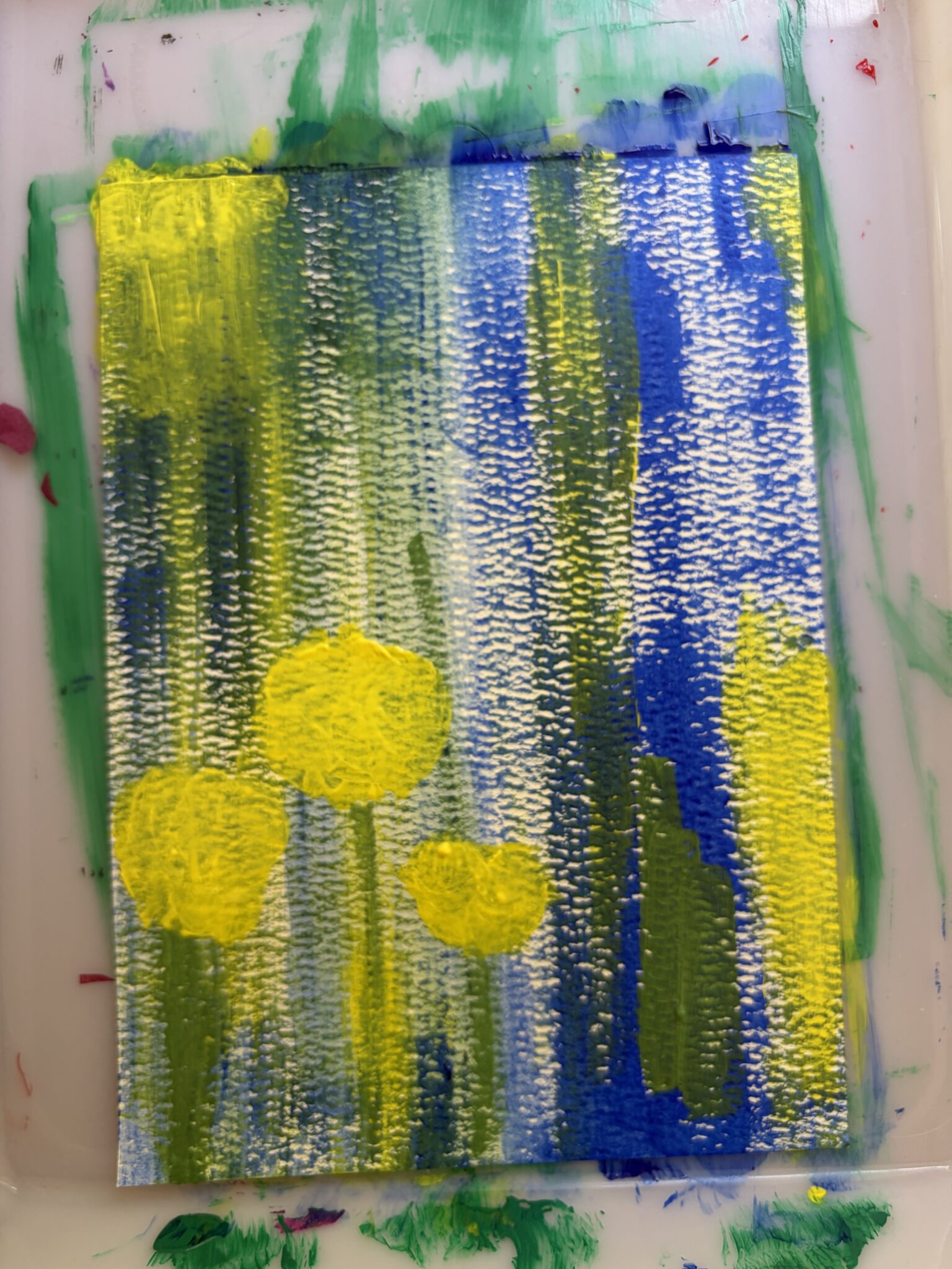 An abstract painting featuring bold vertical brush strokes of yellow and green layered over a blue and white background on paper.